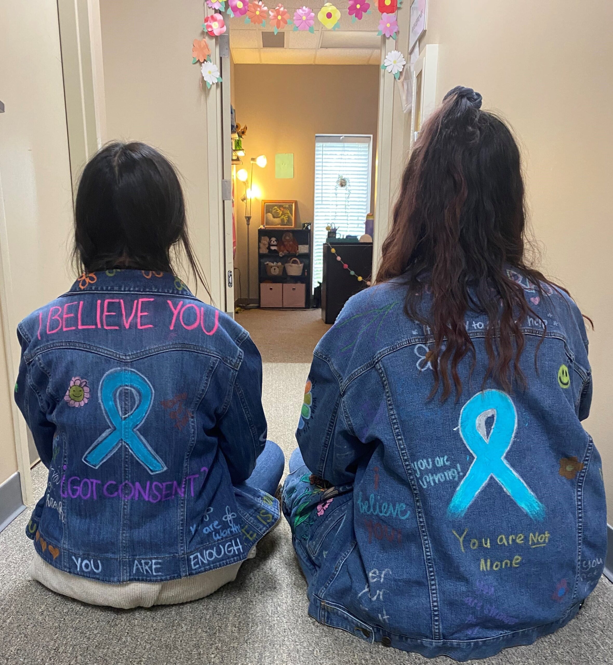 Two women in denim jackets with sexual assault awareness ribbon and phrases