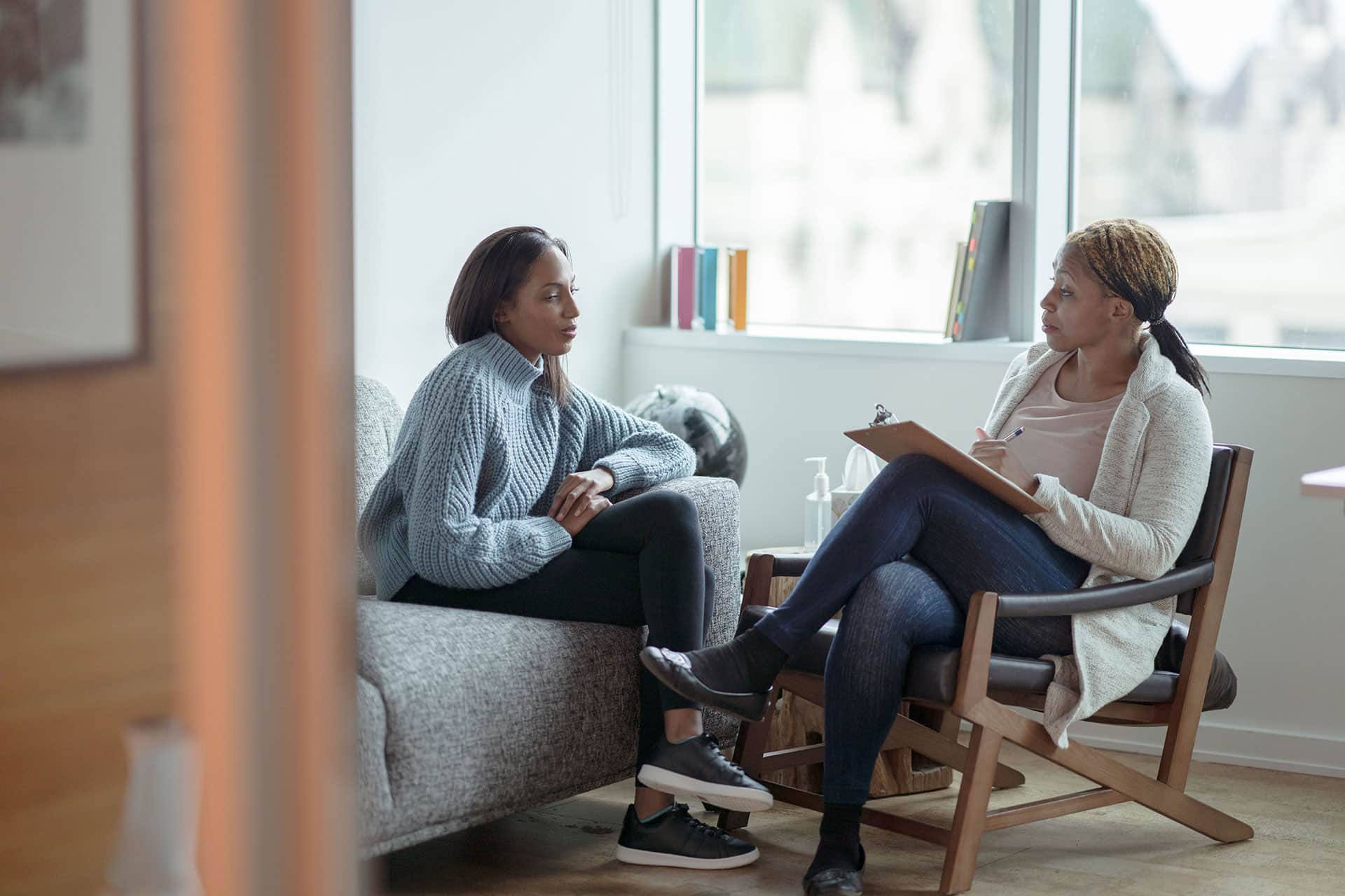 Two women seated talking while one woman takes notes on clipboard
